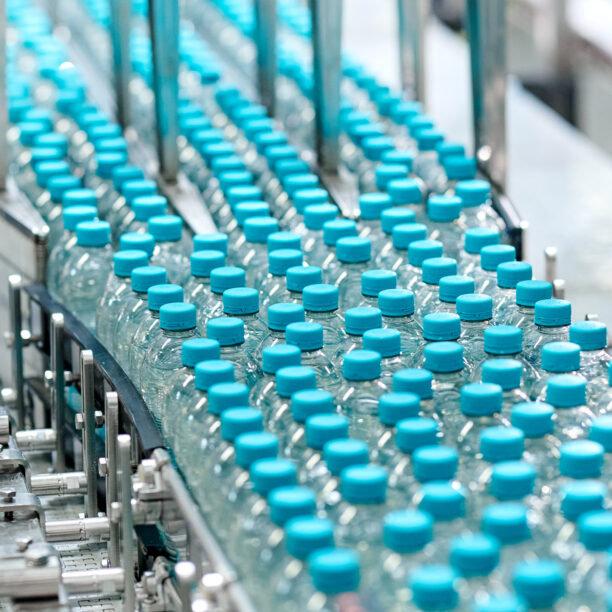 eine Vielzahl von PET Flaschen mit hellblauem Deckel auf einem Fließband